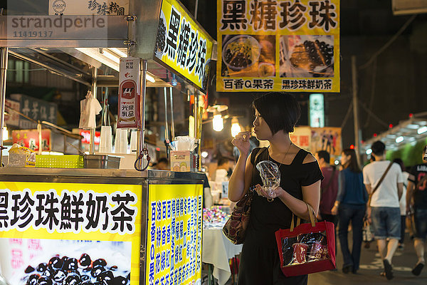 Die lokalen Nachtmärkte von Taipeh sind berühmt für ihr köstliches Essen  eine junge Frau genießt einige Snacks; Taipeh  Taiwan  China'.