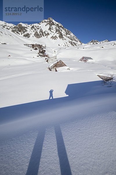 Der Fotograf Doug Lindstrand fotografiert seinen Schatten am Hatcher Pass in der Nähe der Independence Mine im Spätwinter. Im Hintergrund sind die alten  verfallenen Minengebäude im Schnee zu sehen  in der Nähe von Palmer  Süd-Zentral-Alaska; Alaska  Vereinigte Staaten von Amerika'.