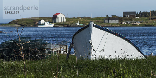 Ein Ruderboot auf dem Grasufer mit Gebäuden und Häusern entlang der Küste  Cape Breton Island; Nova Scotia  Kanada'.