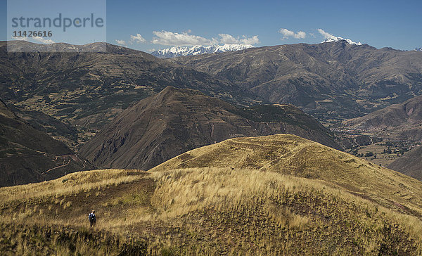 Ein Wanderer bahnt sich seinen Weg durch die Ausläufer der Anden mit den schneebedeckten Gipfeln im Hintergrund der peruanischen Landschaft; Cusco  Peru'