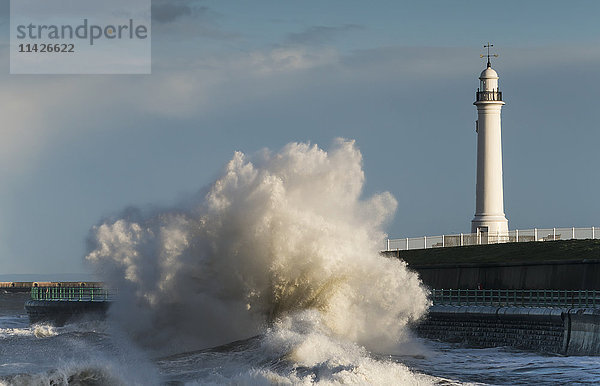 Eine große Welle bricht und kracht gegen das Ufer vor einem Leuchtturm; Sunderland  Tyne and Wear  England'.