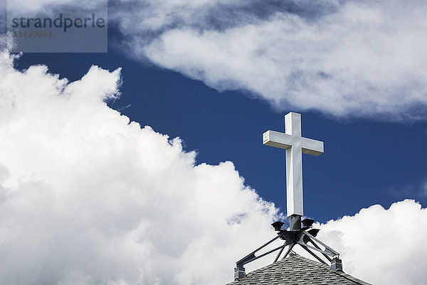 Weißes Kreuz auf einem Spitzdach mit weißen Wolken und tiefblauem Himmel; Calgary  Alberta  Kanada'.