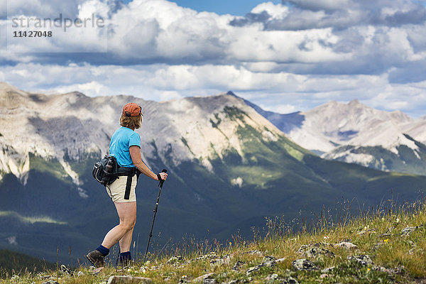 Wanderin auf einem felsigen Hügel mit Blick auf eine Bergkette und ein Tal bei bewölktem Himmel  westlich von Bragg Creek; Alberta  Kanada'.