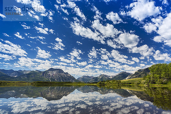 Dramatische Wolken  die sich auf einem ruhigen Bergsee mit einer Bergkette in der Ferne und blauem Himmel spiegeln; Waterton  Alberta  Kanada'.