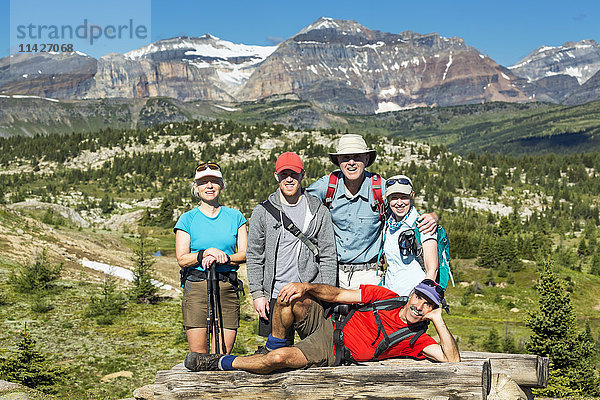 Gruppe von Wanderern  die auf einer Holzbank mit dem Tal unter ihnen und den Bergen und dem blauen Himmel in der Ferne posieren; Banff  Alberta  Kanada'.