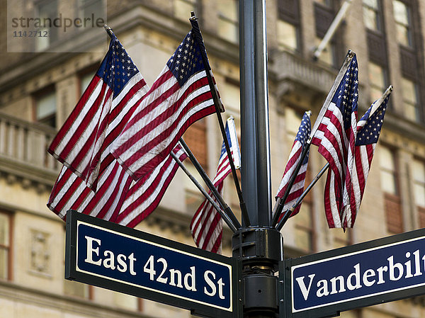 Amerikanische Flaggen auf einem Mast über den Straßenschildern an der Kreuzung von East 42nd Street und Vanderbilt; New York City  New York  Vereinigte Staaten von Amerika