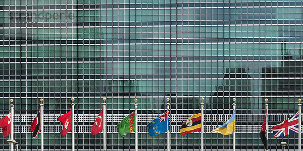 Internationale Flaggen in einer Reihe vor einem Gebäude der Vereinten Nationen mit Glasfassade; New York City  New York  Vereinigte Staaten von Amerika'.