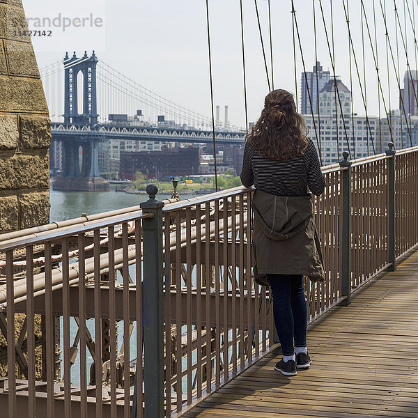 Eine junge Frau steht auf der Brooklyn Bridge und blickt über den East River auf die Manhattan Bridge; New York City  New York  Vereinigte Staaten von Amerika'.