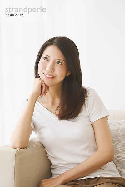 Junge japanische Frau auf dem Sofa in einem weißen Raum