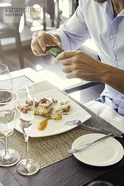 Mann  der sein Essen im Restaurant mit dem Smartphone fotografiert.