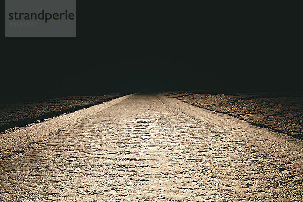 Von Autoscheinwerfern beleuchtete unbefestigte Straße in der Wüste  Death Valley National Park  USA