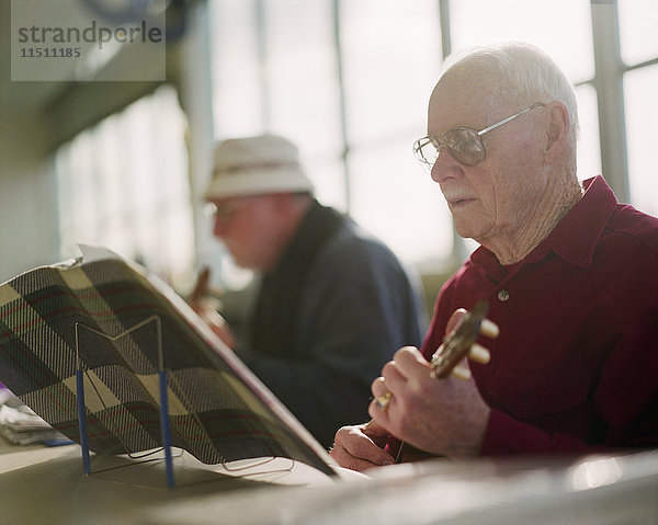 Zwei ältere Männer spielen Ukulele-Instrumente in einem Seniorenzentrum.