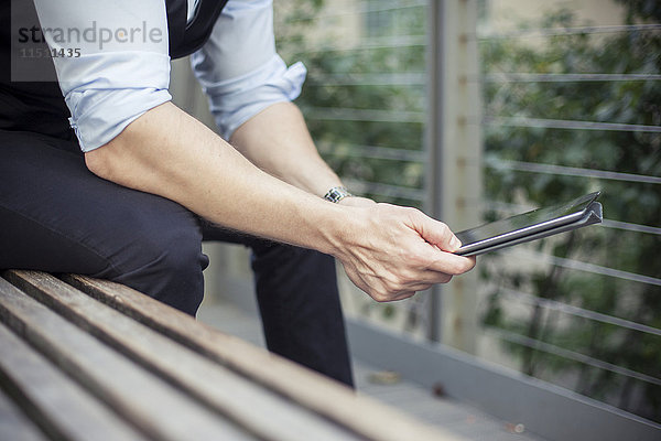 Mann auf Bank sitzend  mit digitalem Tablett  beschnitten