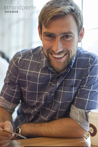 Mann sitzt im Café mit Kreditkarte in der Hand und lächelt fröhlich.