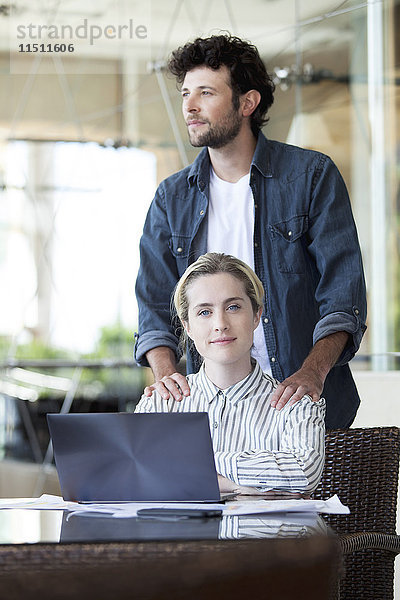 Mann massiert die Schultern der Frau  während sie am Laptop arbeitet.
