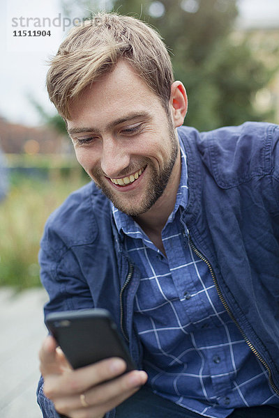 Junger Mann SMS mit Smartphone im Freien