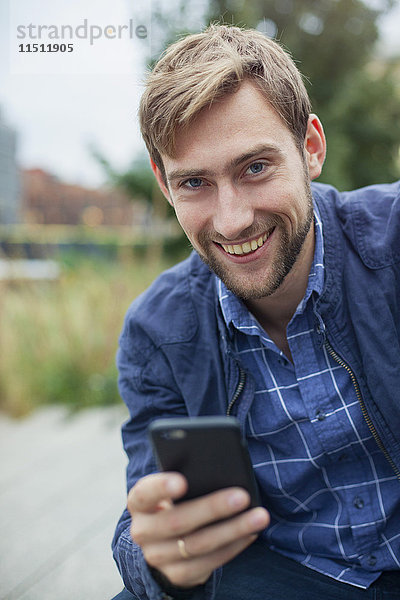 Mann mit Smartphone im Freien  lächelnd  Portrait