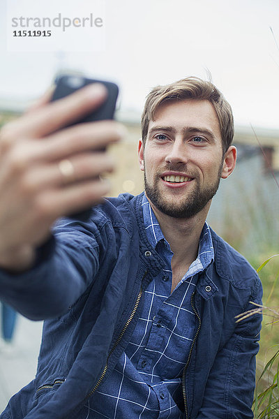 Mann  der ein Smartphone benutzt  um einen Selfie zu nehmen.