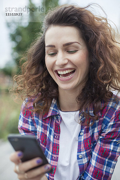 Junge Frau lacht  während Textnachrichten im Freien gesendet werden