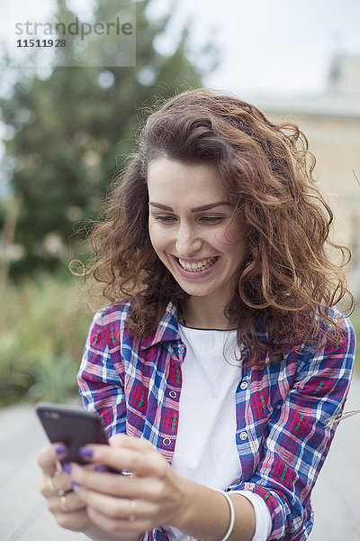 Fröhliche junge Frau mit Smartphone im Freien