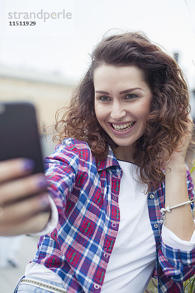 Junge Frau  die ein Smartphone benutzt  um einen Selfie zu nehmen.