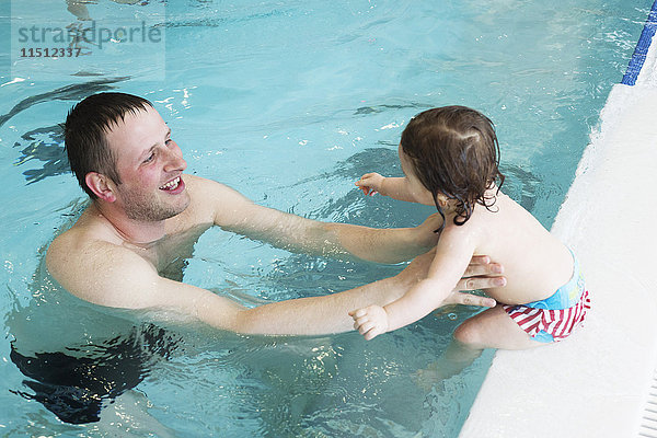 Kleines Mädchen  das mit Hilfe der Eltern schwimmen lernt.