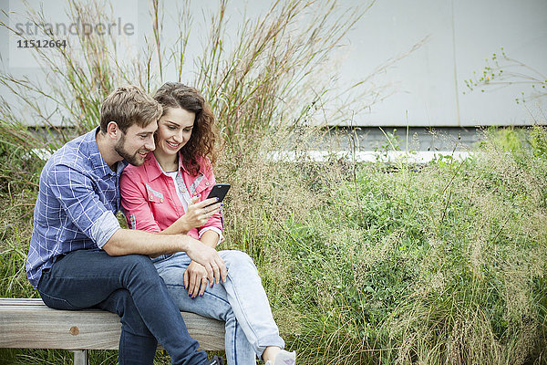 Paar sitzt zusammen auf der Parkbank und schaut auf das Smartphone.