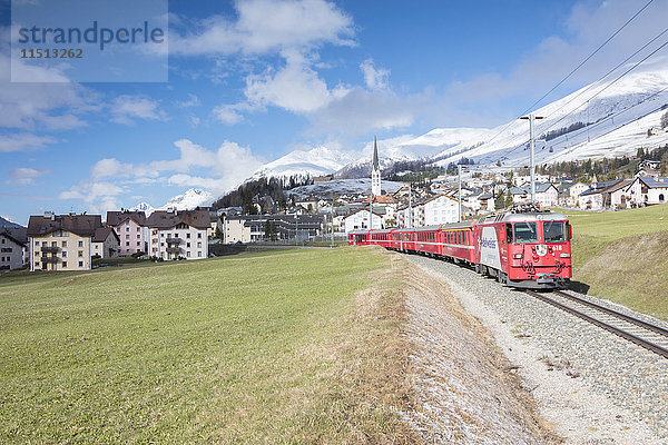Der rote Zug fährt im Frühling durch das Alpendorf Zuoz  Maloja  Kanton Graubünden  Engadin  Schweiz  Europa