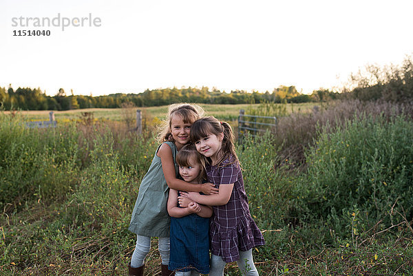 Porträt von drei jungen Mädchen  die zusammen im Feld stehen und sich umarmen