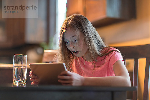 Junges Mädchen benutzt digitales Tablett am Küchentisch