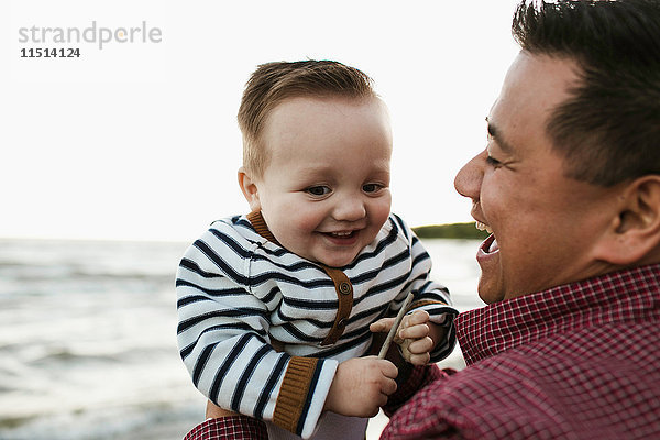 Vater am Strand hält lächelnden kleinen Jungen