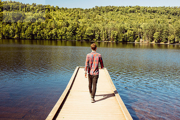 Mann geht am Holzsteg des Sees entlang  Rückansicht