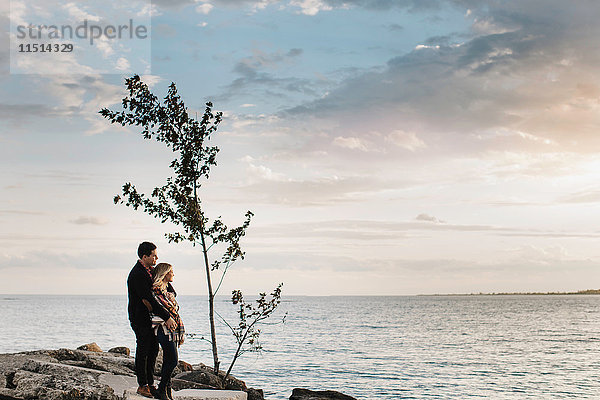 Junges Paar steht auf Felsen am Meer und schaut auf die Aussicht