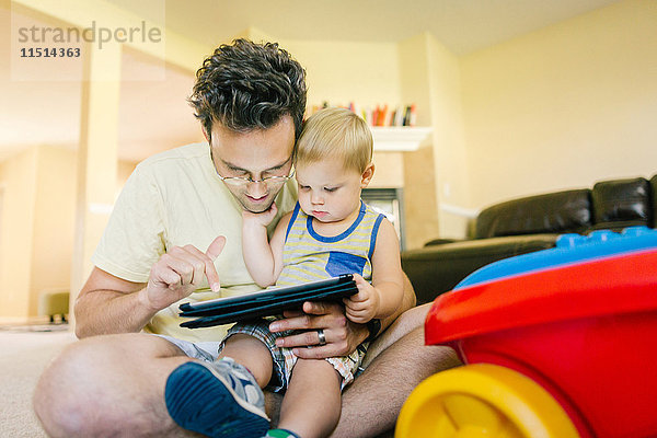 Vater und kleiner Sohn spielen zu Hause zusammen und schauen sich ein digitales Tablet an