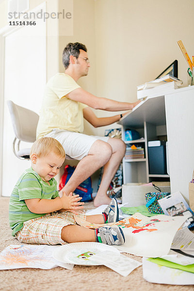 Vater benutzt Computer  während der kleine Sohn auf dem Boden spielt