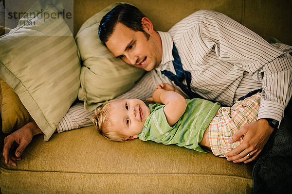 Vater und kleiner Sohn liegen zusammen auf dem Sofa