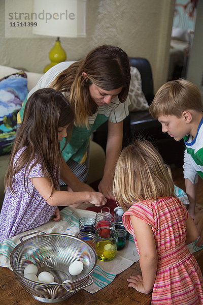 Mutter und drei Kinder färben Ostereier bei Tisch