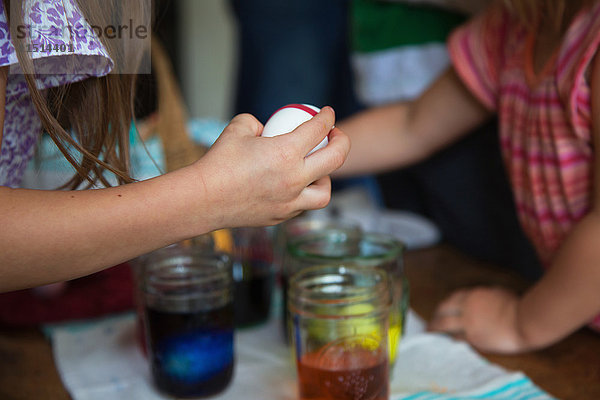 Hände von zwei jungen Schwestern  die sich bei Tisch darauf vorbereiten  Ostereier in Gläsern zu färben