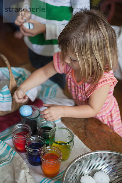 Mädchen und Bruder färben Ostereier in Gläsern bei Tisch
