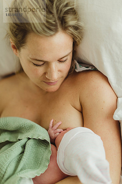 Draufsicht einer mittleren erwachsenen Frau  die eine neugeborene Tochter im Bett stillt