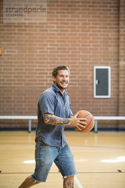 Tätowierter Mann hält Ball beim Üben auf dem Basketballplatz