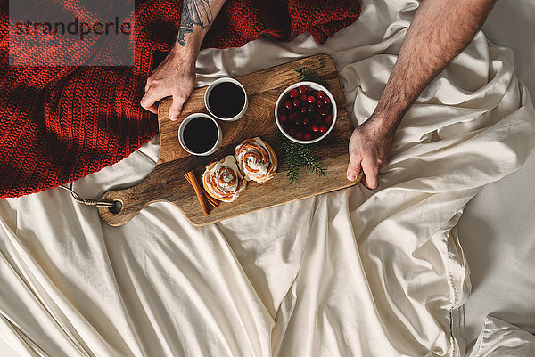 Draufsicht auf männliche Hände  die das Frühstück für zwei im Bett halten