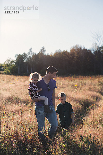 Junger Mann spaziert mit Tochter und Sohn bei Sonnenuntergang über das Feld