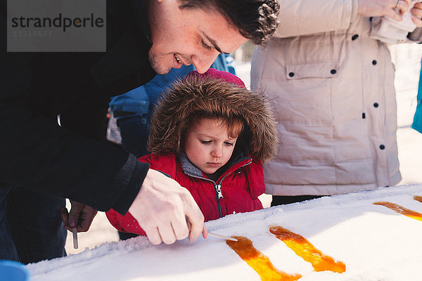 Mädchen in Pelzkapuze mit Vater beim Lollymachen im Schneeeis