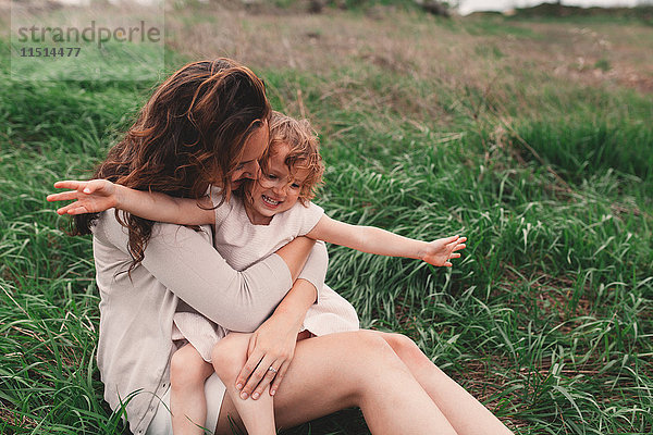 Mädchen sitzt auf dem Schoss der Mutter auf windigem Feld