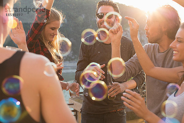 Erwachsene Freunde spielen mit schwebenden Blasen auf Dachterrassenparty