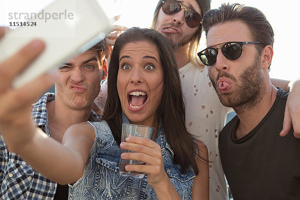 Junge erwachsene Freunde ziehen auf Dachterrassen-Party Gesichter für Selfie