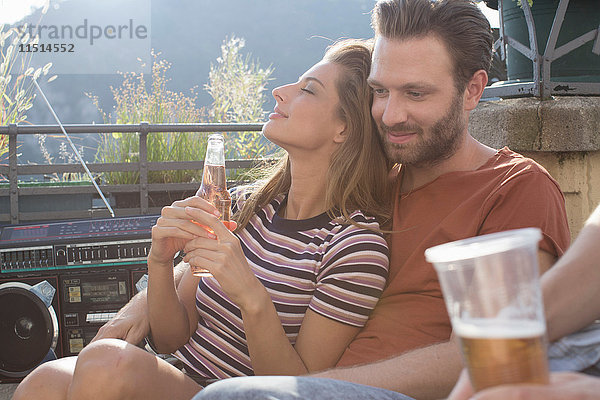 Junge Frau entspannt sich auf der Dachterrassenparty auf dem Schoß ihres Freundes