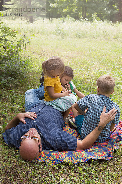 Vater und Kinder entspannen sich auf einer Decke im Gras