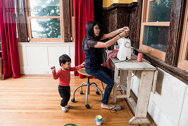 Männliches Kleinkind spielt  während die Mutter an der Nähmaschine arbeitet.